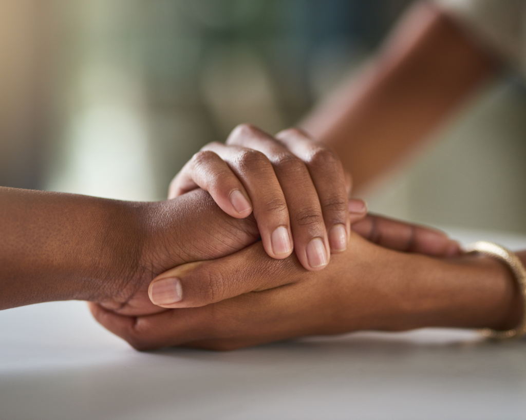 Two people grasp hands over a tabletop in emotional support.