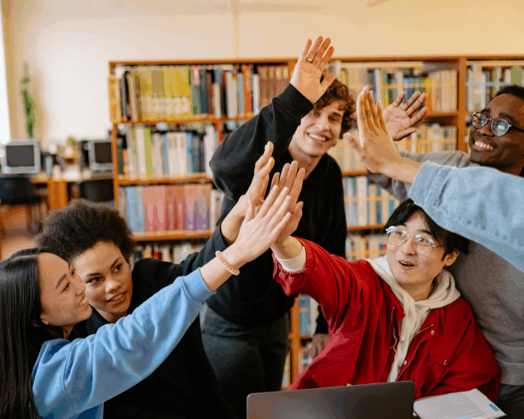 Diverse group of college students high-fiving over a table in a library