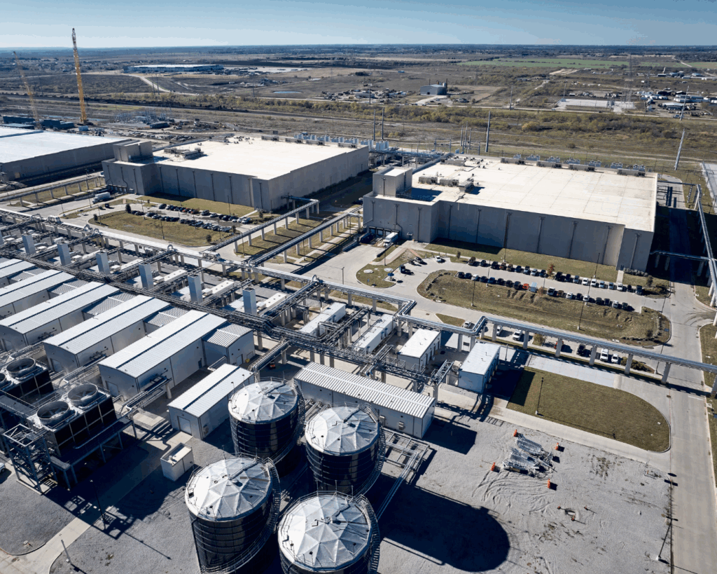 An aerial photograph of a Google data center in Texas, showing three large buildings, a row of generators, and four large water storage tanks.