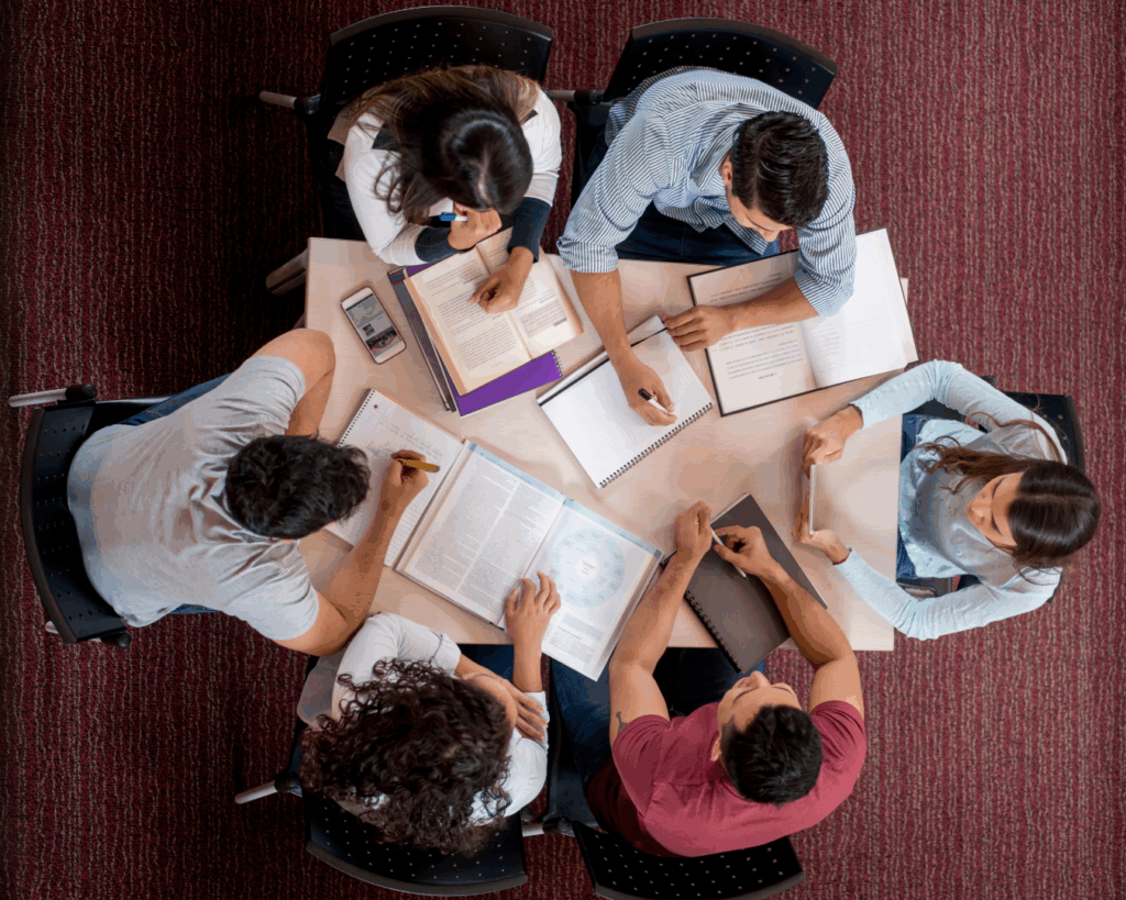 Birds-eye photo of a group of students working around a small table, with books and papers scattered between them.