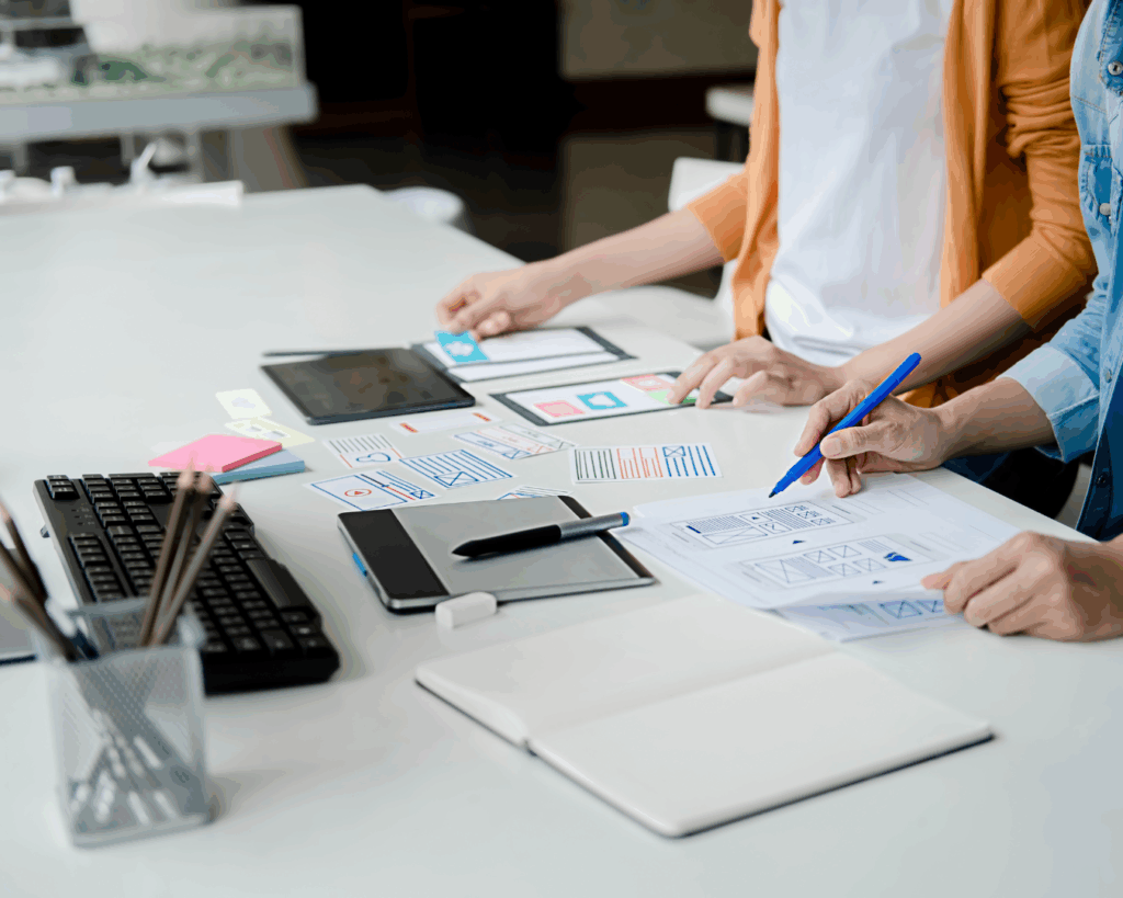 Photo of the hands of two web designers working together, discussing hand-drawn wireframes and UX sketches.