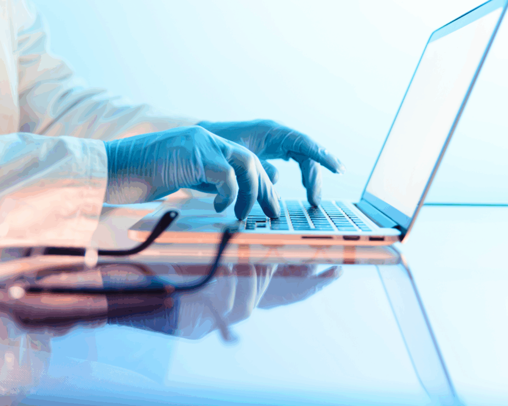 Dramatically lit close-up photo of a scientist's blue-gloved hands typing on a laptop.