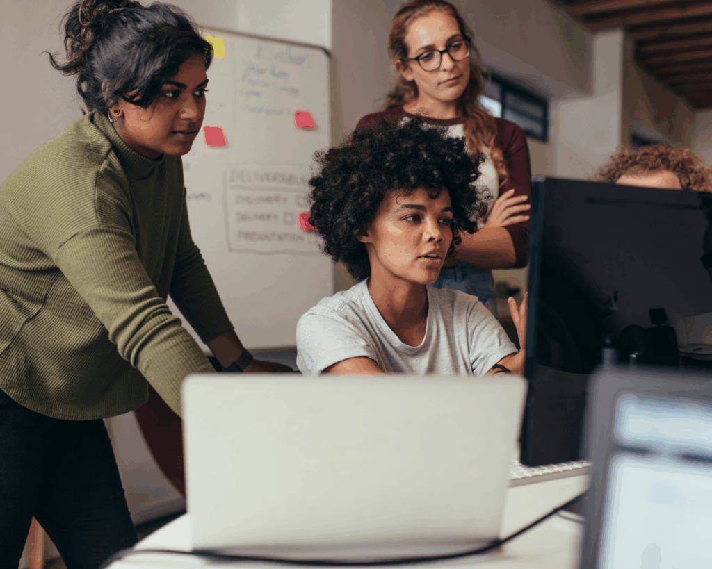 Photo of a team of professionals working together at a desk with several computers.