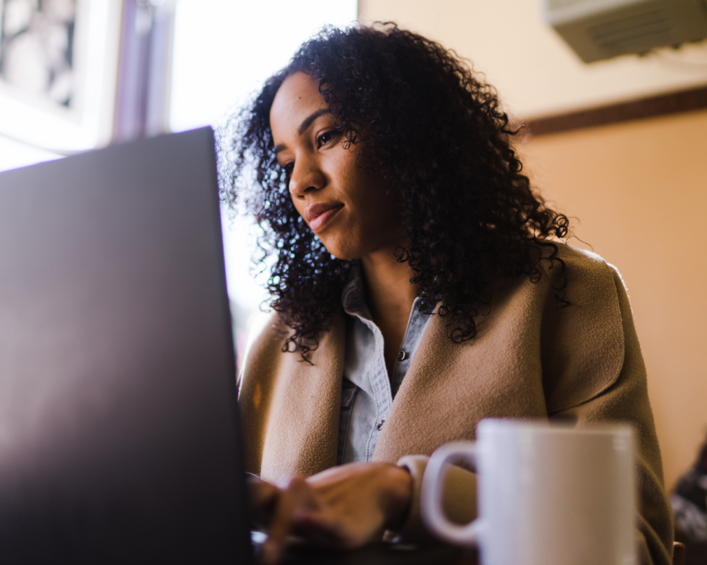Low-angle photo of a professionally dressed woman sitting at a desk and working on a laptop.