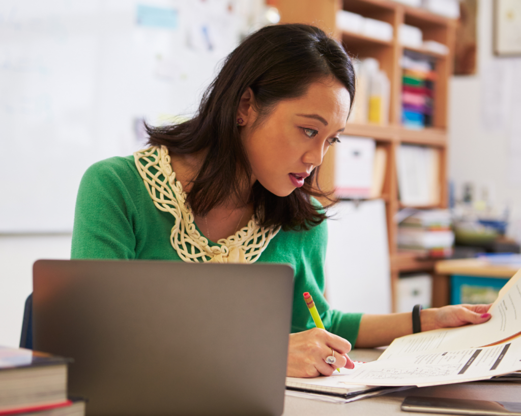 Photo of a young teacher working on papers in front of her laptop